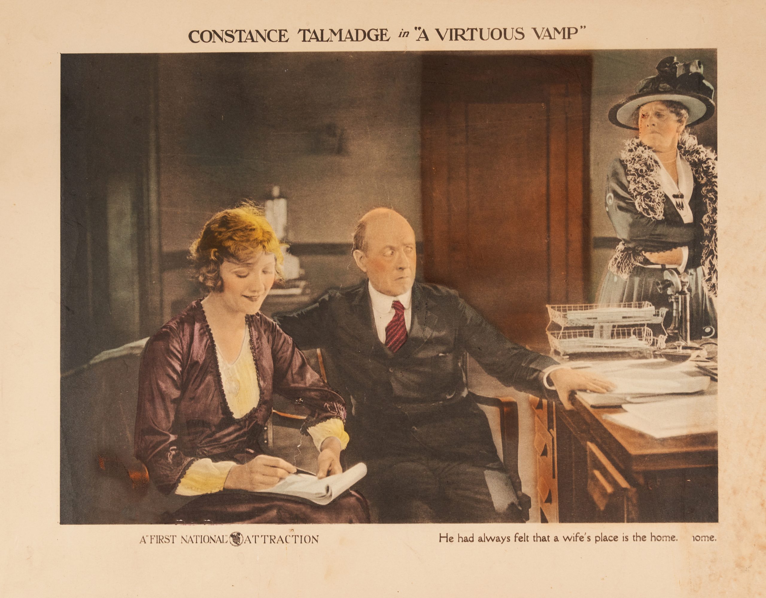 A colored-in lobby card showing a younger woman and her nervous boss whose wife looks on disapprovingly.