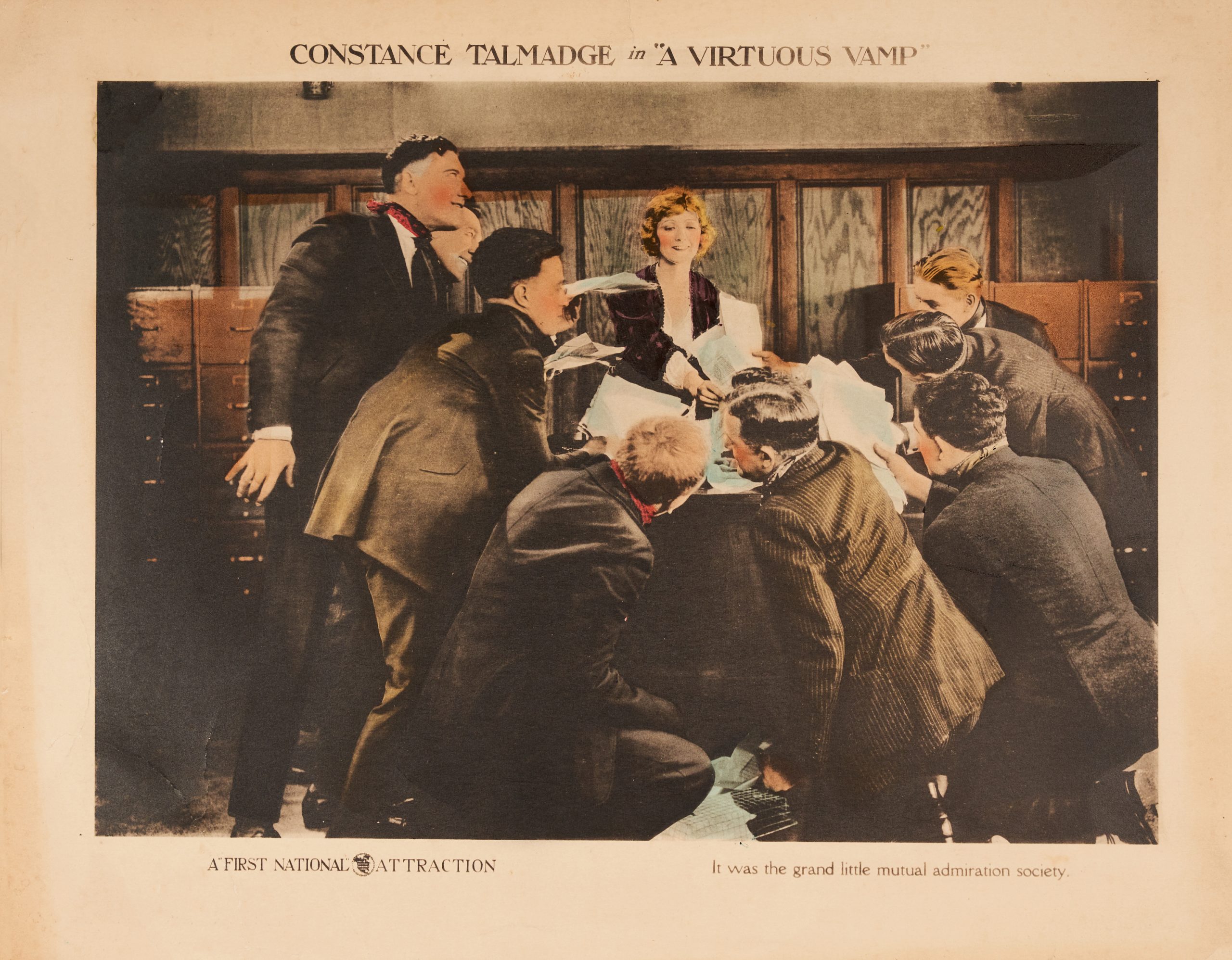A colored-in lobby card showing a young woman in an office surrounded by men eager to give her paperwork.