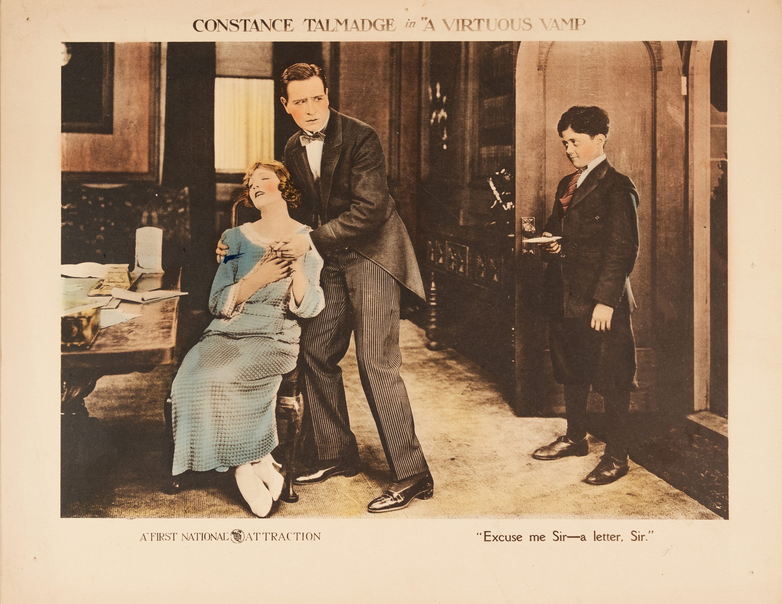 A colored-in lobby card showing a man comforting a woman. An office boy catches them touching in a way in a familiar way.