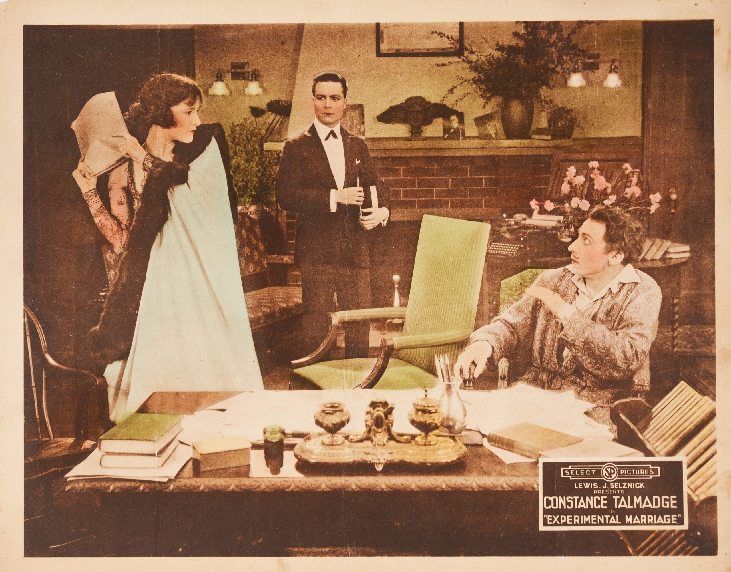 A colored-in lobby card of two men looking anxiously at a woman. She holds papers in her hand as if to strike.
