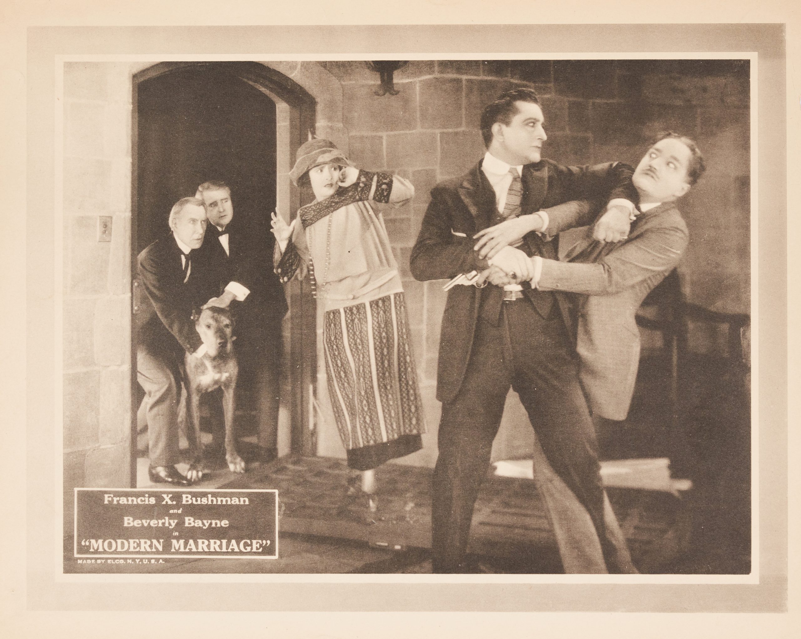 A lobby card showing two men fighting while a woman recoils and two other men hold back a dog.