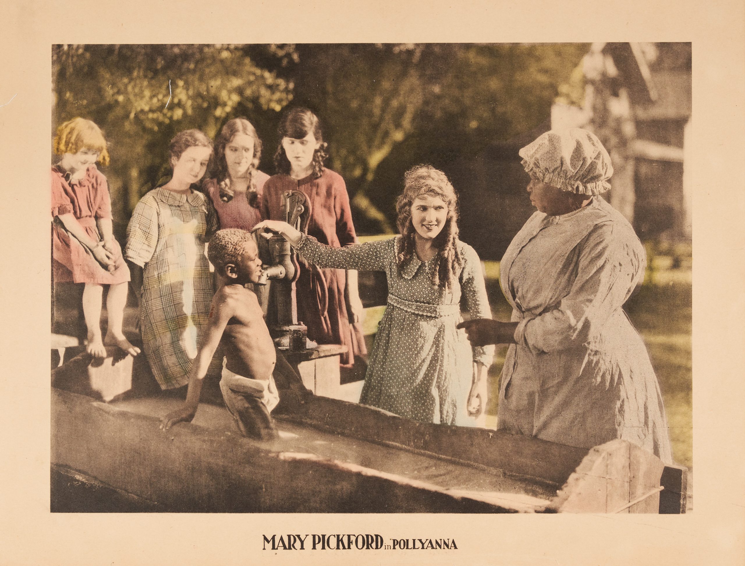 A colored-in lobby card with Mary Pickford as Pollyanna pulling a young boy's hair by a haystack.