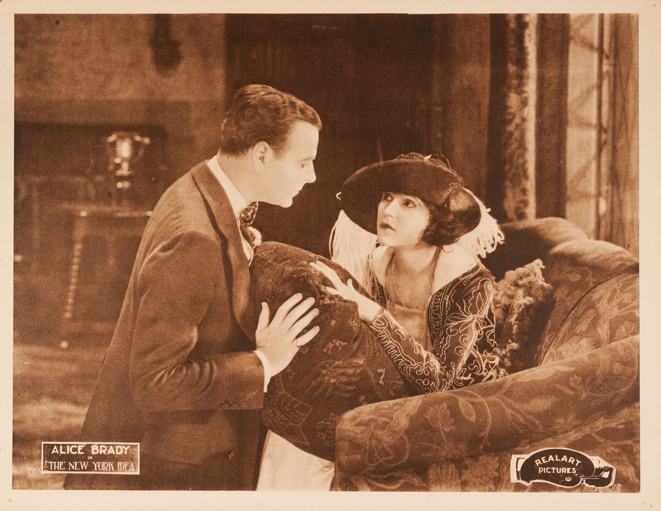 A sepia lobby card showing a man and woman looking intensely at each other on the couch.