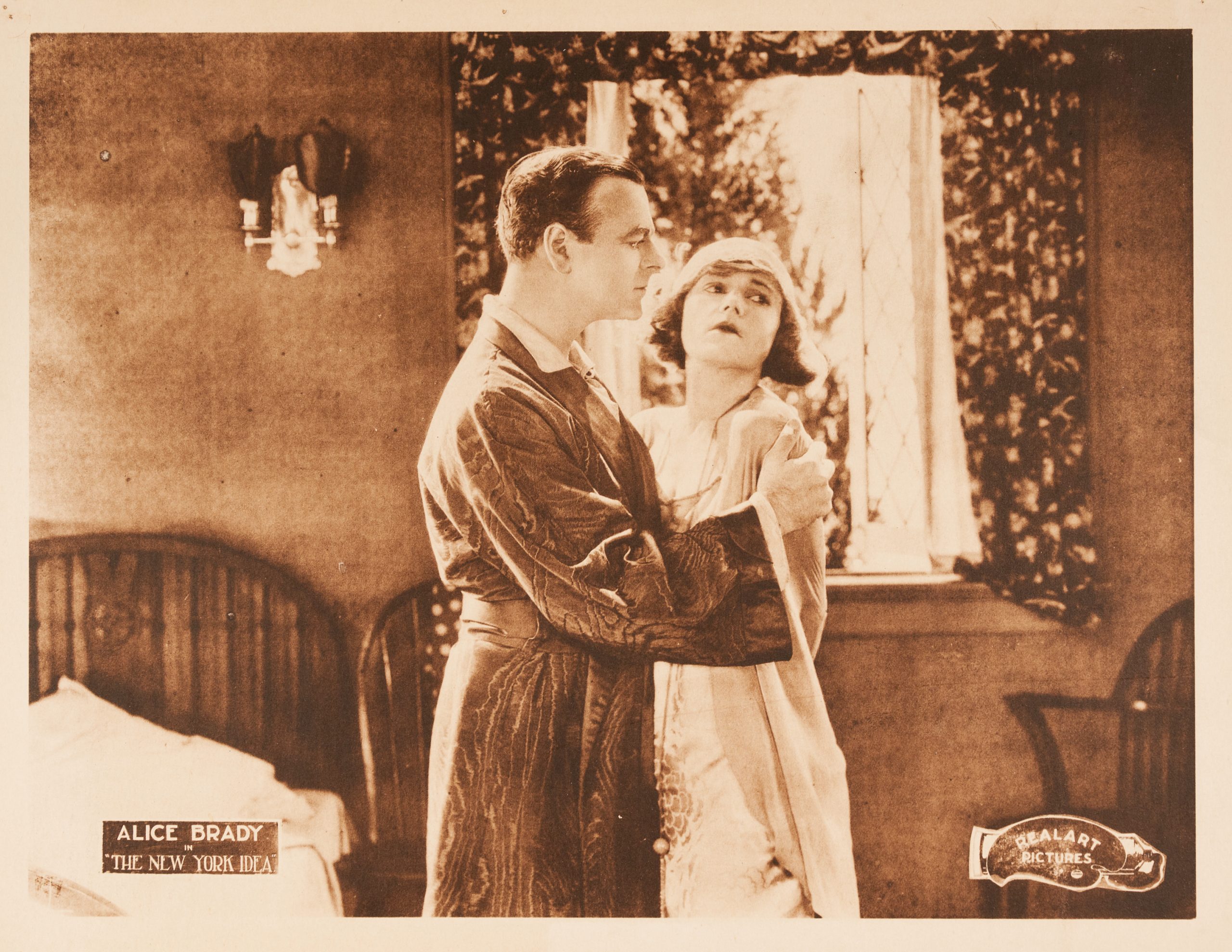 A sepia lobby card of a man reassuring a forlorn-looking woman with an embrace.