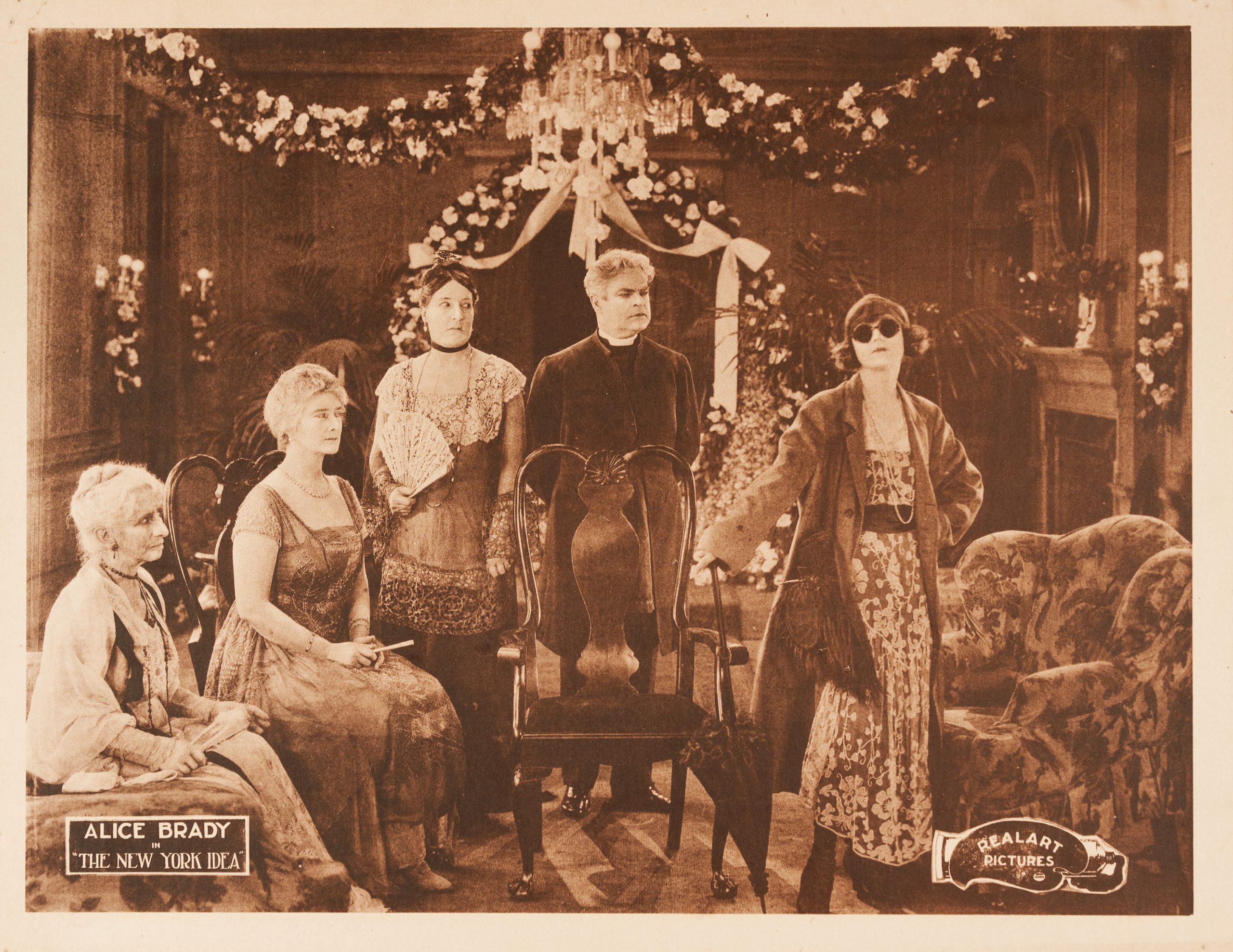 A sepia lobby card showing a group of adults looking disapprovingly at a self-posessed woman in sunglasses.
