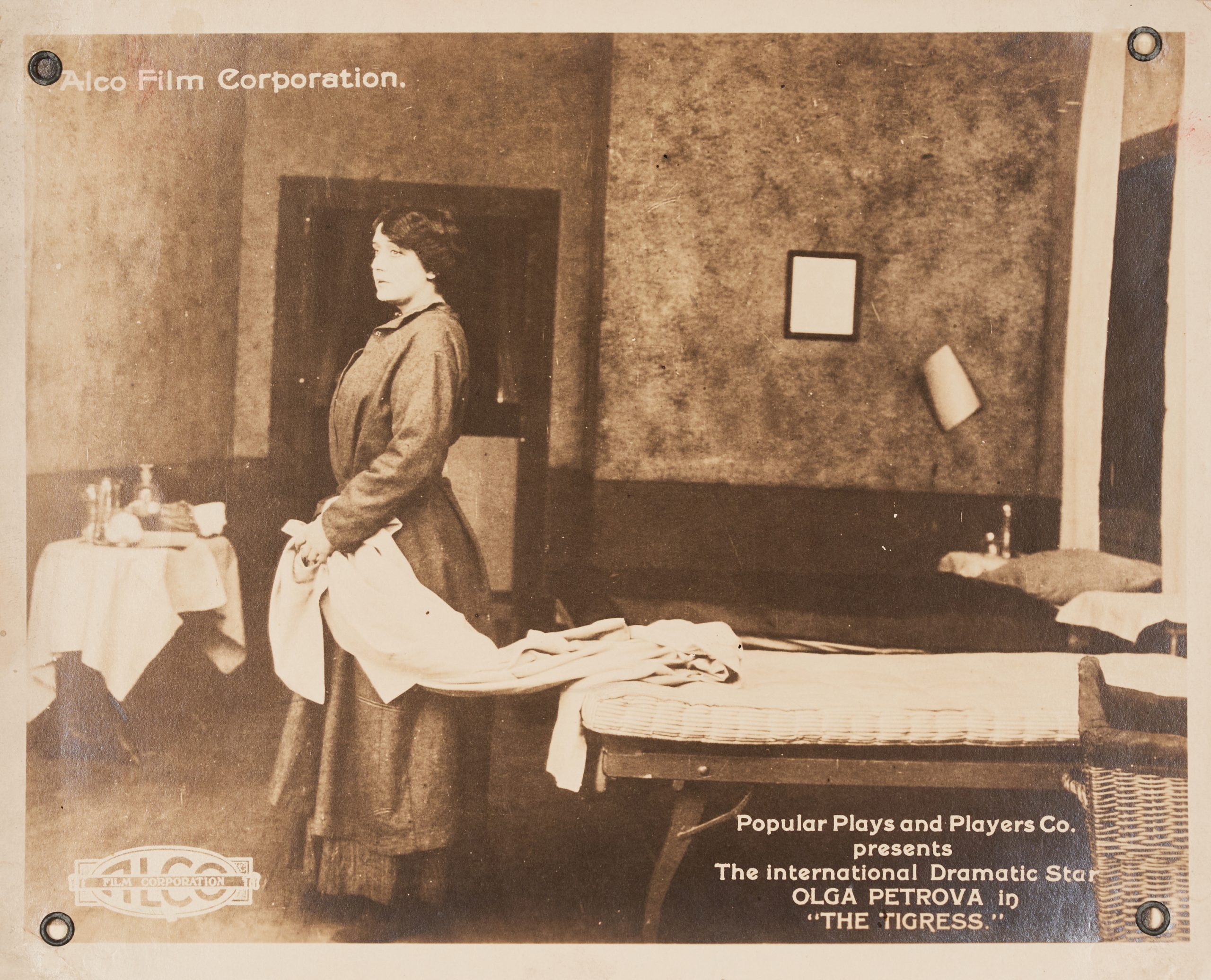A publicity photograph of a scene with a woman holding bed linens and looking off into the distance.