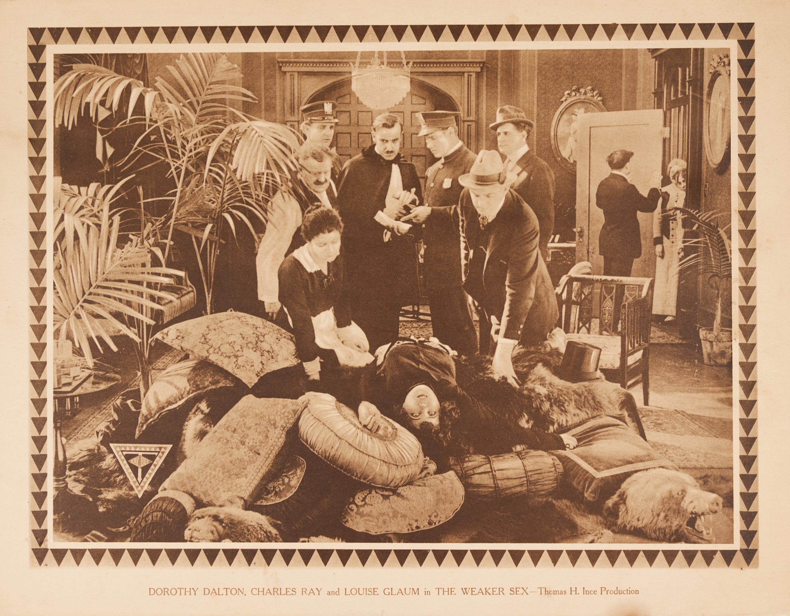 A sepia-toned lobby card with a woman lying dead on a pile of pillows as a crowd stands over her.