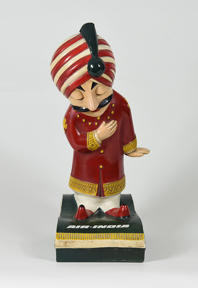 A figurine of mustachioed figure wearing a turban. His hand is over his heart as he bows.