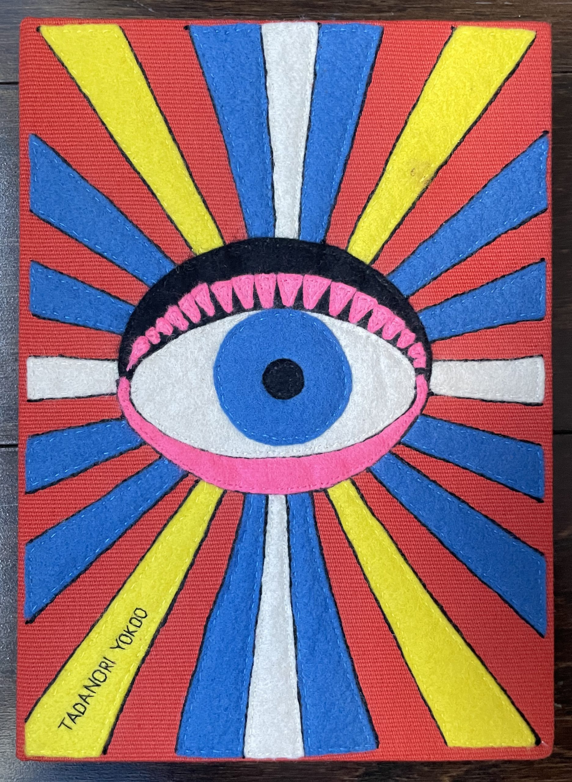 A purse of an eyeball in the center with colorful rays coming from it.